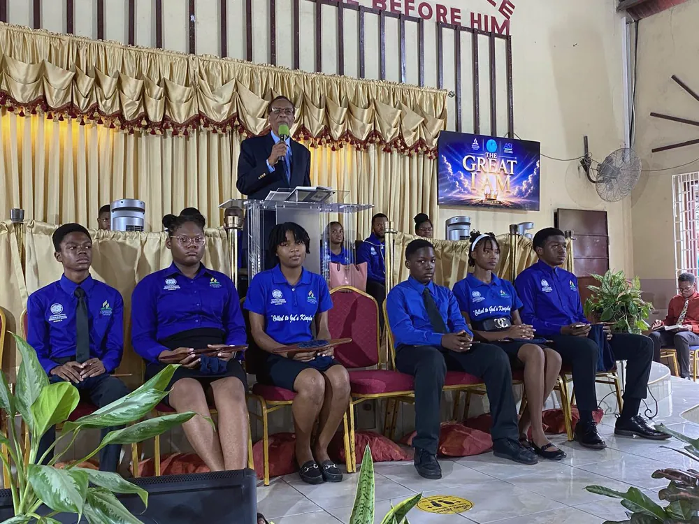 Members seated on the platform beneath the Great I Am title screen